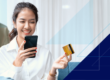Woman smiling at cell phone while holding her credit card after using mobile wallet while online shopping